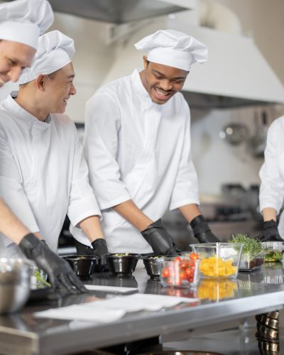 Multiracial team of cooks mixing ingredients for take away food in professional kitchen